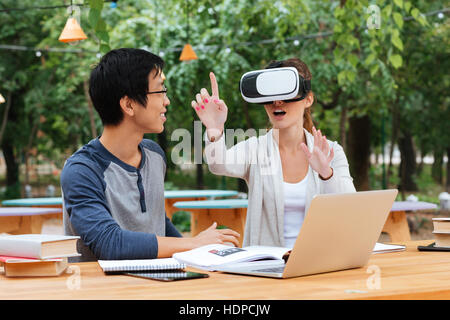 Two cheerful young students studying and using virtual reality glasses outdoors Stock Photo
