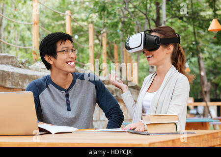 Smiling young couple of student sitting and using virtual reality glasses outdoors Stock Photo