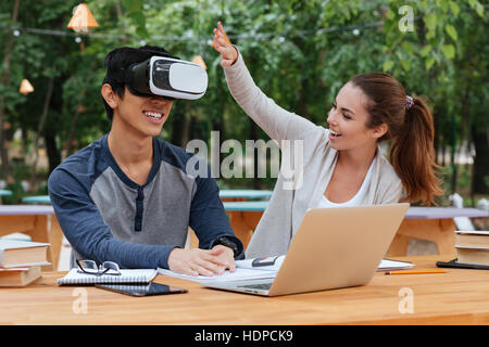 Happy young couple with virtual reality glasses using laptop and having fun outdoors Stock Photo