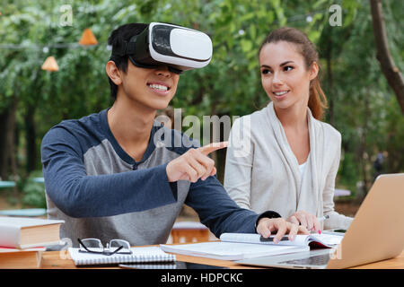 Happy young couple using virtual reality glasses and pointing away outdoors Stock Photo