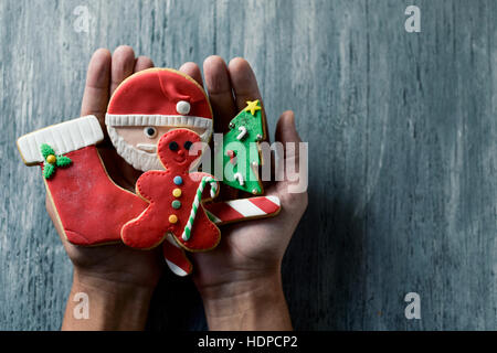 closeup of a young caucasian man with a pile of christmas cookies with different shapes and colors in his hands, against a rustic wooden surface, with Stock Photo