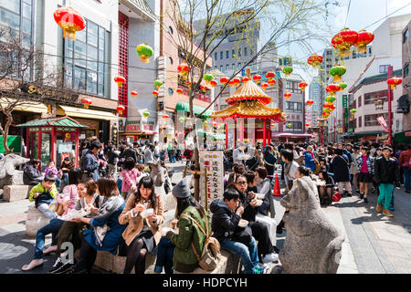 Japan, Kobe, Nankinmachi, Chinatown. Popular public square with pagoda. Busy with people queueing for restaurants, and others sitting in sunshine. Stock Photo