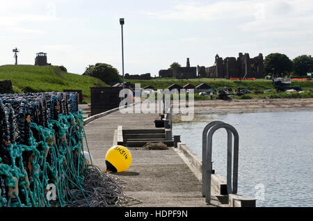 Lobster pots piled-up at the harbour at Lindisfarne (Holy) Island in Northumberland, England, with priory in the distance. Stock Photo