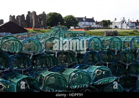 Lobster pots piled-up near the harbour at Lindisfarne (Holy) Island in Northumberland, England, with priory in the distance. Stock Photo