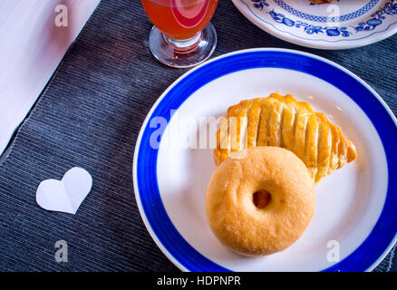 donut and bagel stuffed hot and steaming gold color ready for your breakfast or your own snack with glass of orange juice and a small paper heart Stock Photo
