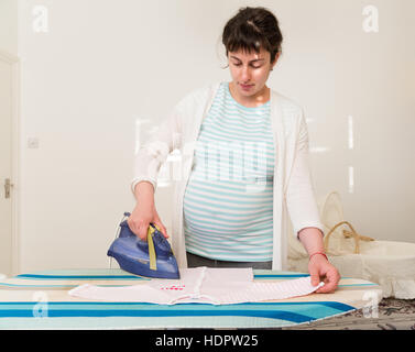 Pregnant woman ironing baby clothes in preparation for baby's arrival, England, UK Stock Photo