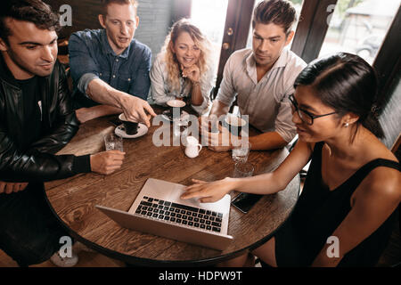 Diverse group of friends sitting together at cafe with man pointing at laptop. Five young people hanging out at a coffee shop Stock Photo