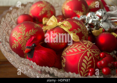 A close photo of a realistic cardinal decoration and decorative Christmas balls in a crystal bowl, featuring the words 'Joy to the world.' Stock Photo