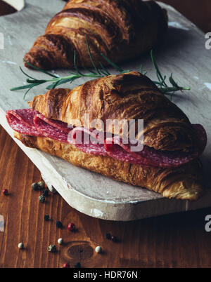 fresh brown croissant with salami on rustic table Stock Photo