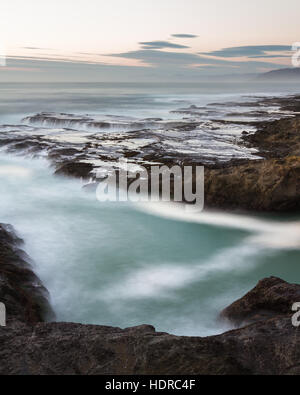 rough seas captured with a slow shutter speed creating a relaxing scene with water flowing over the lava rock with a smooth motion effect Stock Photo