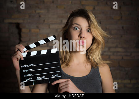 Young blonde girl grimace face and posing with movie clapper board for actress audition Stock Photo