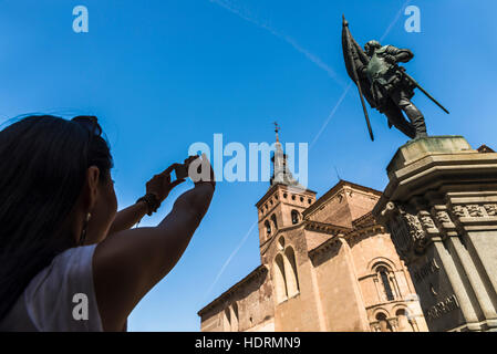 An asian young woman taking a picture of San Martin Church and Juan Bravo statue, Romanic style construction; Segovia, Castilla Leon, Spain Stock Photo