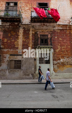 Men walking in synchronicity with each other and the movement of the washing on the balcony above, La Havana, Cuba. Stock Photo