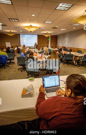 At a Los Angeles seminar for schoolteachers, a student follows along with the lecturer using a laptop computer. Note computer image on lecture screen. Stock Photo