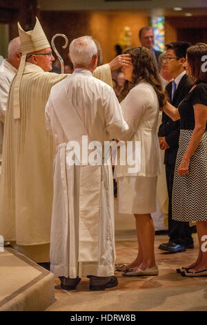 Accompanied by their parents, formally dressed teens participate in Confirmation mass at a Laguna Niguel, CA, Catholic church before a robed bishop. Stock Photo