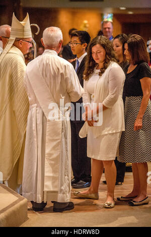 Accompanied by their parents, formally dressed teens participate in Confirmation mass at a Laguna Niguel, CA, Catholic church before a robed bishop. Stock Photo
