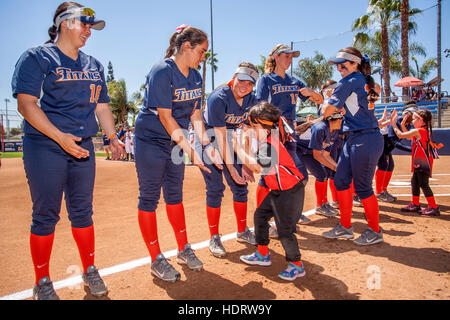 Multiracial college women's softball players trade hand slaps with a little girl admirer as they prepare for a game on the field in Fullerton, CA. Stock Photo