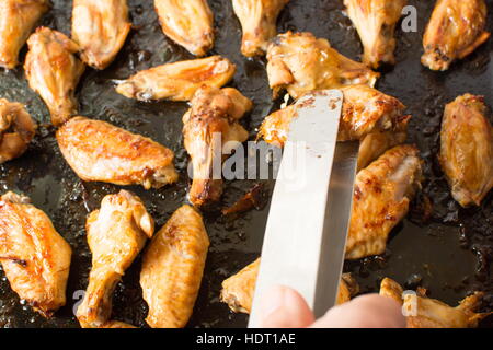 Cooking tongs holding bbq chicken wings on black plate Stock Photo