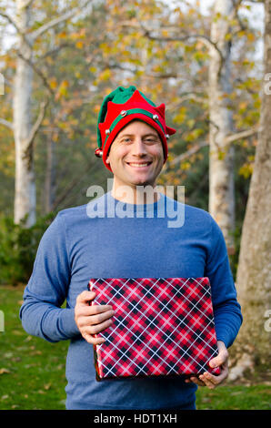 Man holding a Christmas present wearing a Christmas hat. Stock Photo