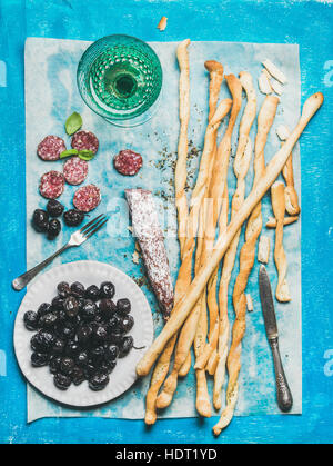 Grissini bread sticks, sausage, olives and white wine, blue background Stock Photo
