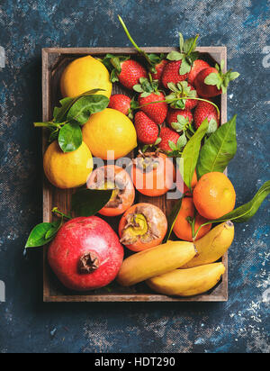 Oranges, lemons, pomegranate, bananas, strawberries and persimmon in wooden box Stock Photo