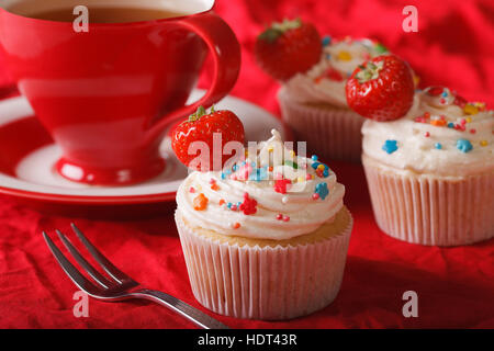 Beautiful cupcakes with cream and fresh strawberries and a cup of tea on the table. Horizontal close-up Stock Photo