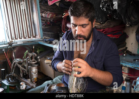 A man repairs shoes in a booth on a sidewalk in Yazd, Yazd Province, Iran Stock Photo