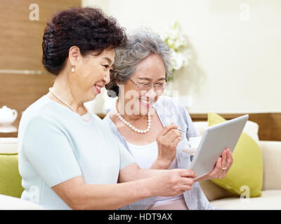 side view of two senior asian women sitting on couch taking a selfie using mobile phone, happy and smiling Stock Photo