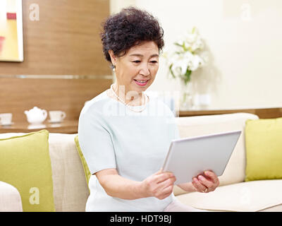 senior asian woman sitting on couch looking at tablet computer Stock Photo