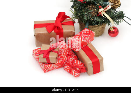 Christmas presents with red ribbons and bows in front of a christmas tree against a white background Stock Photo