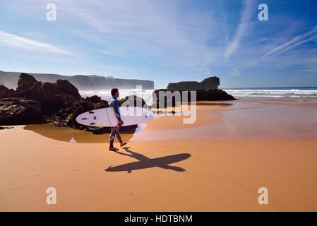 Surfer walking with his board towards the ocean at rocky beach with ebb tide Stock Photo