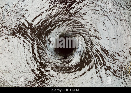 Water vortex / drain / draining away /liquid spiraling down a hole ( like a plug hole / plughole ) in an unseen water feature. Stock Photo