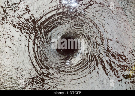 Water vortex / drain / draining away /liquid spiraling down a hole ( like a plug hole / plughole ) in an unseen water feature. Stock Photo