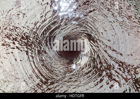 Water vortex / drain / draining away /liquid spiraling down a hole ( like a plug hole / plughole ) in an unseen water feature. Stock Photo