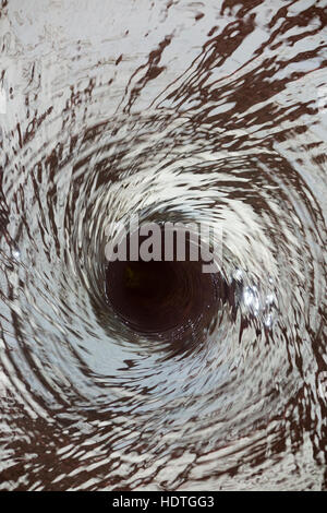 Water vortex / drain / draining away /liquid spiraling down a hole ( like a plug hole / plughole ) in an unseen water feature. Stock Photo