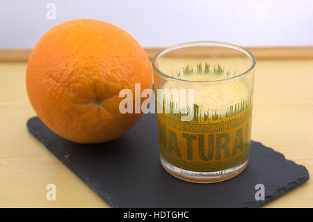A glass of freshly squeezed orange juice with the word Natural written on it. Next to an orange ready to be squeezed. Stock Photo