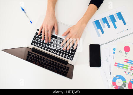 Laptop with women hand and paper graph on white table. Stock Photo