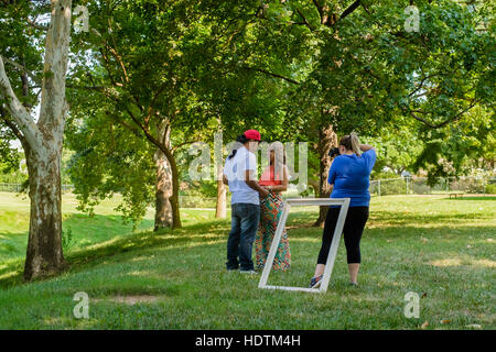 An ethnic couple pose while a female photographer takes their picture outdoors in a park. Oklahoma City, Oklahoma, USA. Stock Photo