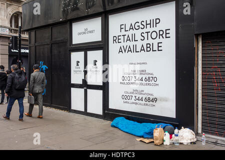 Homeless person sleeping outside an empty retail unit on Oxford Street in London, UK Stock Photo