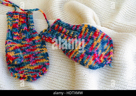 Two multicolored knitted mittens on white scarf. Close-up. Stock Photo