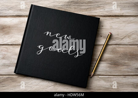 high-angle shot of a pencil and a notebook with the text new goals written in its cover, on a rustic wooden surface Stock Photo
