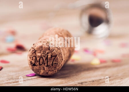 the number 2017, as the new year, written in the cork of a bottle of champagne, on a wooden table full of confetti Stock Photo