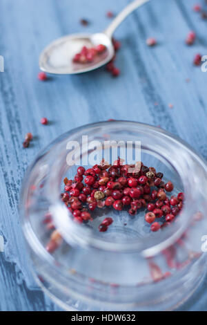 Pink pepper in glass jar on blue background Stock Photo