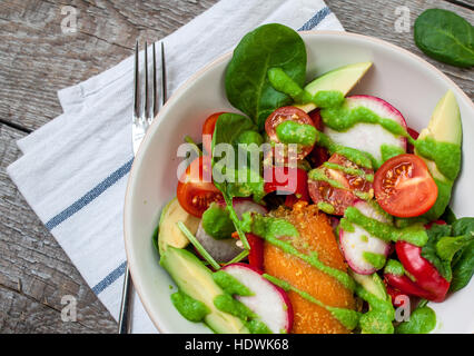 Green salad with spinach, pesto, sweet potato, avocado, radishes, peppers, tomatoes. Love for a healthy raw food concept.