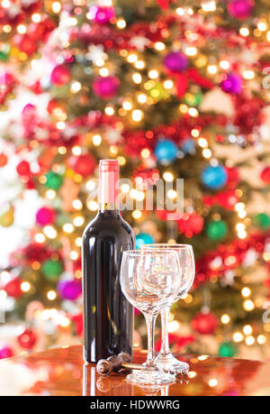 Empty drinking glasses, vintage cork screw and unopen wine bottle on Mahoney table with bright Christmas tree lights in background.  Vertical format l Stock Photo