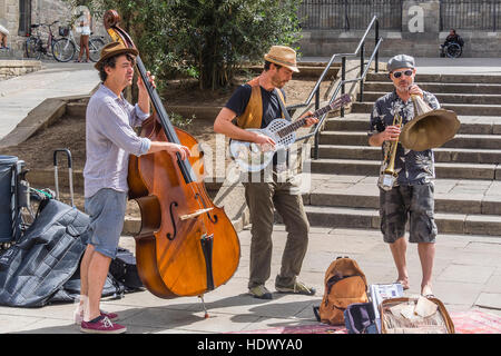 A trio of street musicians perform for the public in a plaza in Barcelona, Spain. They include a bass player, a guitarist and a trumpeter. Stock Photo