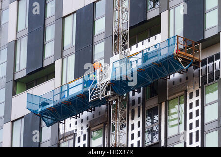 Construction worker on gantry fitting facia panels to new build flats, Liverpool, UK Stock Photo