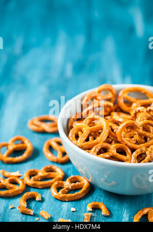Salty snacks mini pretzels in bowl on blue wooden table Stock Photo