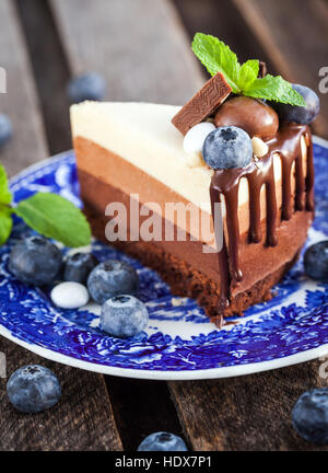 Piece of delicious three chocolate mousse cake decorated with fresh blueberry, mint and candies Stock Photo