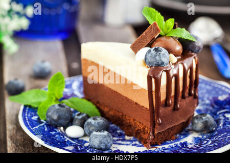 Piece of delicious three chocolate mousse cake decorated with fresh blueberry, mint and candies Stock Photo